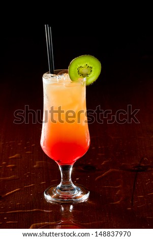 sex on the beach, fresh orange juice with vodka and cherry juice served in a stem glass on a dark bar