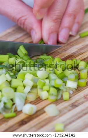 closeup of hand in motion slicing  fresh clean leeks or green onions on a cutting board