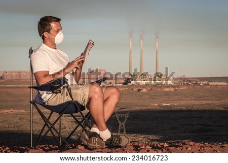 concept image of a man sitting reading a book wearing a mask with a coal power plant and dirty smoke in the background