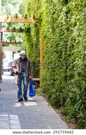 Calistoga, California - May 08 : Elderly gentleman walking down an ally with a shopping bag and drinking a can of soup thru a straw, May 08 2015 Calistoga, California.