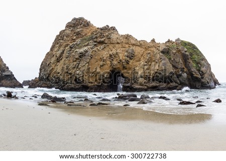 Large rock on the beach with a tunnel where the waves come in and out creating a natural feature and attraction