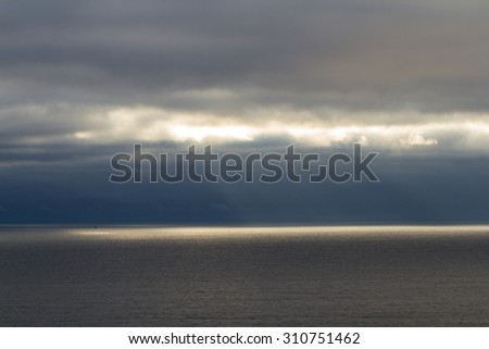 tranquil seascape of the pacific ocean in central Oregon with dark clouds and fog being penetrated by bright sun rays