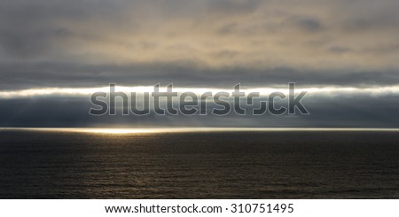 tranquil seascape of the pacific ocean in central Oregon with dark clouds and fog being penetrated by bright sun rays