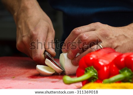 close up of a chefs hands slicing fresh mozzarella cheese with red bell peppers in the foreground