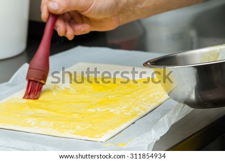 close up of a food grade brush spreading an egg mixture over a thin pastry dough