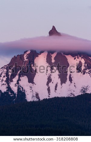 Mount Thielsen at sunset with a reddish glow and a  lingering fog around the tip of the mountain