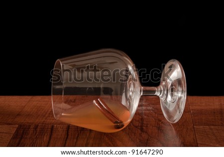 Snifter laying sideways on a bar top isolated on a black background with a cinnamon stick inside and a liquor