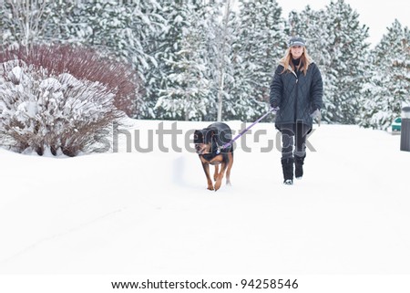 caucasian woman walking a black dog in snow covered path