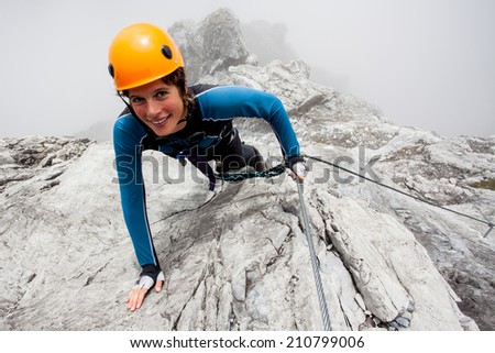 Young woman climbing steep rock wall