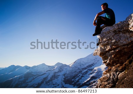 Young man sitting on rock above mountain range