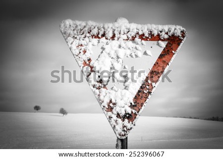 give way road sign, traffic sign, yield sign, with blue sky and clouds and with snow in winter season