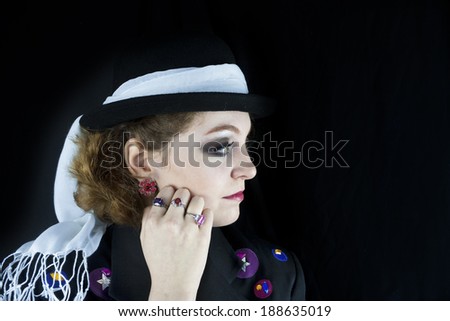 Profile of beautiful young woman wearing hat with white scarf and jacket with leather and rhinestone details.
