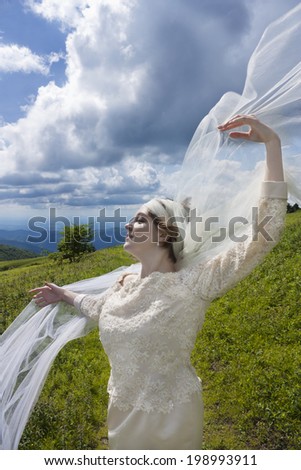 Young bride with long veil blowing in the wind on mountain top