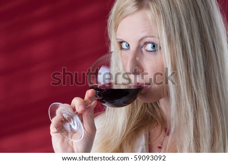 Portrait of a beautiful young woman with a glass of red wine. She tastes wonderful red wine and looking to you (into camera).