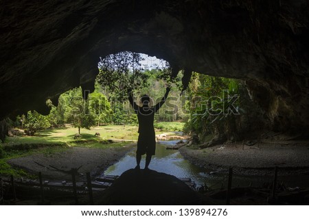 Man standing with arms raised inside Tham Loed cave with stalactites in Mae Hong son, North Thailand