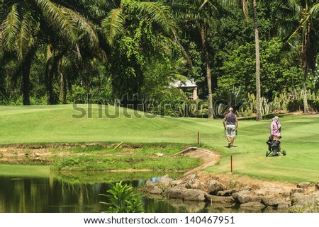 Senior male golfer walking with caddie to green on 4th hole on Green Valley/St Andrews golf course near PAttaya, Thailand