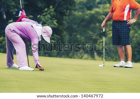 Senior male golfer and caddie on green at 4th hole on Green Valley/St Andrews golf course near Pattaya, Thailand