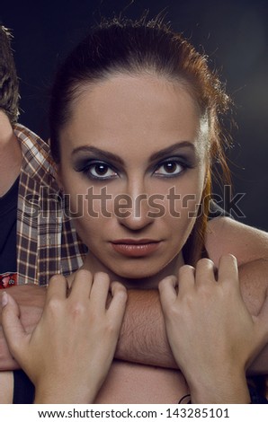 Couple of lovers. The guy holding the girl\'s neck, hugging her tightly. The girl with two hands holding a hand guy and looking at the camera. On a black background