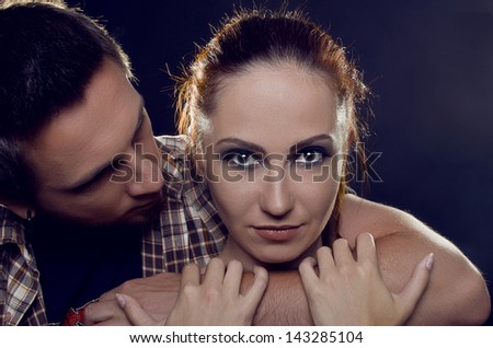 Couple of lovers. The guy holding the girl's neck, hugging her tightly, looking at her. The girl with two hands holding a hand guy and looking at the camera. On a black background