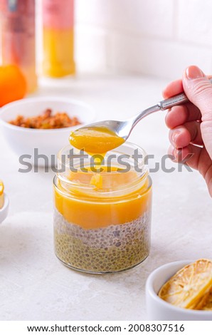 Jar of chia seeds and mango jam. A woman is eating a healthy dessert from a jar with a teaspoon. Pleasant appetizing snack - tender mus Zdjęcia stock © 