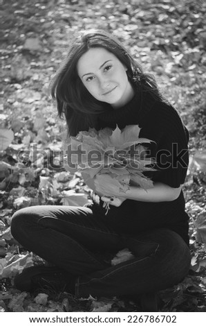 Beautiful woman sitting on the fallen leaves with a bouquet of maple leaves
