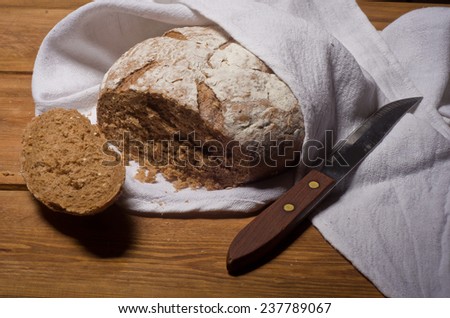 Rosy loaf of bread wrapped in white linen towel lying on a wooden table