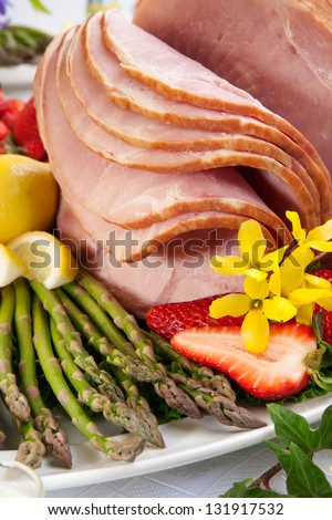 Festive glazed ham for Easter celebration dinner garnished with asparagus, carrots, strawberry, and lemon wedges.