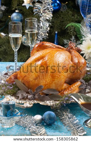 Roasted turkey garnished with herbs on blue Christmas decorations, and champagne. Christmas tree as background.