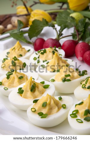 Plate of deviled eggs, fresh radish, Easter decoration eggs, and fresh spring blooming tulips.