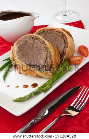 Beef Wellington - delicious roasted beef tenderloin rolled in mushroom puree and prosciutto, then wrapped in puff pastry. Garnished with green beans, tomatoes, and asparagus.
