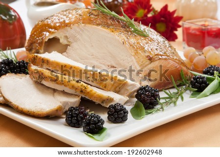 Carved Rosemary-basil rub roasted turkey breast garnished with grapes, blackberies, and fresh basil, and rosemary in fall themed surrounding.