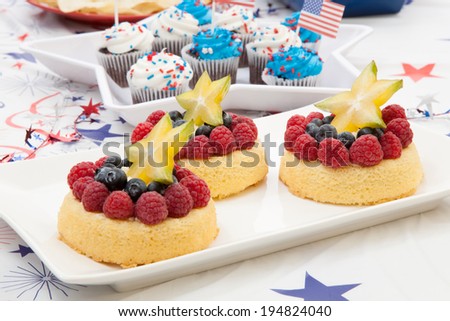 Tray of fresh Angel food fruit cakes with raspberry, blueberry, and star fruit. Muffins on 4th of July in patriotic theme in background.