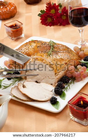 Carving Rosemary-basil rub roasted turkey breast garnished with grapes, blackberies, and fresh basil, and rosemary in fall themed surrounding.