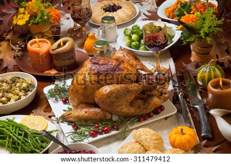 Roasted turkey garnished with cranberries on a rustic style table decoraded with pumpkins, gourds, asparagus, brussel sprouts, baked vegetables, pie, flowers, and candles.