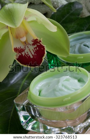 Closeup of two jars of cosmetics cream and blooming Cymbidium orchid flowers for everyday use.