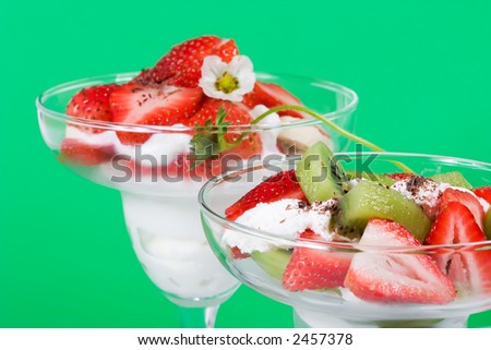 Closeup of martini glass full of fresh kiwi, strawberries, banans and cream with organic yogurt sprinkled by chocolate crumbles over green paper background