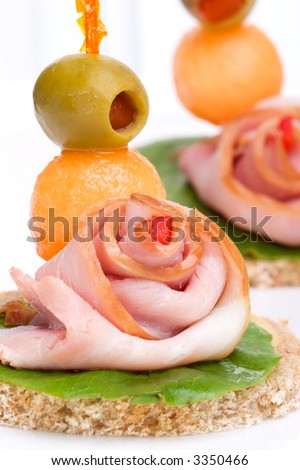 Closeup of delicious ham and melon canapes-sandwiches made from ham, melon green salad and olive over white background
