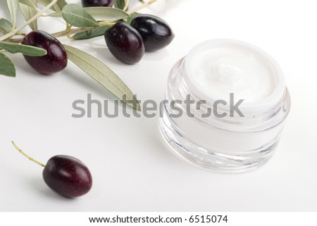Closeup of jar of moisturizing face cream and twig with black olives.