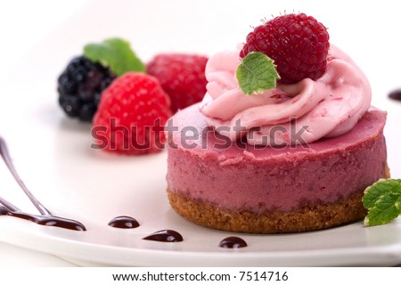 Closeup of delicious raspberry cheesecake served with fresh raspberries, blackberries, mint and chocolate syrup
