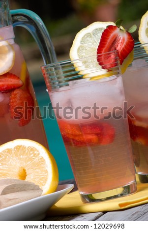Closeup of two glasses of home made iced cold pink strawberry lemonade and pitcher on hot summer on edge of swimming pool.