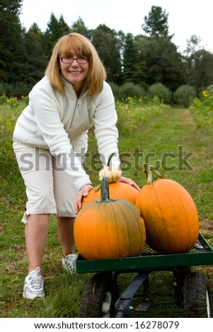 Blond smiling woman picking up pumpkins at pumpkin patch