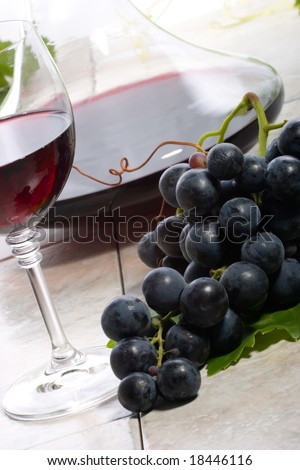 Glass of red wine, decanter and fresh cut black wine grape bunch.