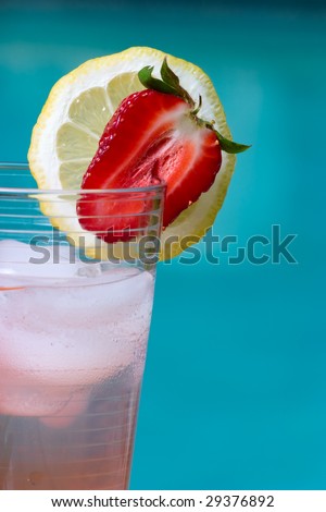 Closeup of glass of home made iced cold lemonade on hot summer on edge of swimming pool.