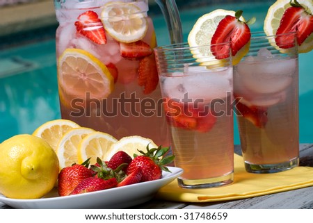 Two glasses of home made iced cold pink strawberry lemonade and pitcher on hot summer on edge of swimming pool.