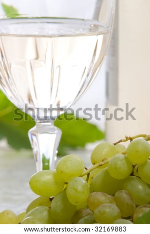 Glass of white wine, bottle and fresh cut green grape bunch.