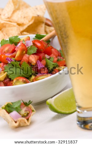 Bowl with fresh cherry tomatoes and avocado salsa. Corn chips and beer. Very shallow DOF on salsa.
