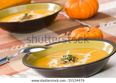 Two bowls of hot delicious pumpkin soup garnished with cream, roasted pumpkin seeds and fresh thyme