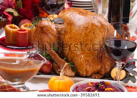 Garnished roasted turkey on holiday decorated table with pumpkins and glasses of red wine