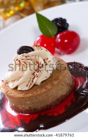 Delicious Cappuccino Cheesecake on chocolate-cherry syrup served with fresh blackberries, maraschino cherry and mint. Christmas ornament out of focus in background