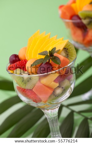 Two servings of fresh tropical fruit salads in cocktail glass. Kiwi, melon, papaya, mango, red grapes, strawberry and chocolate mint.